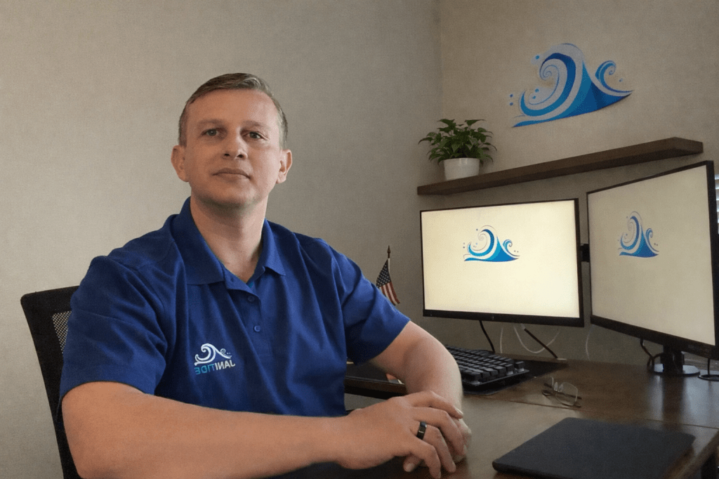 Janitide founder sitting at his office desk in Orlando, Florida, wearing branded cleaning service uniform with dual monitors and company logo in the background.